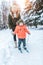 Young mother insures supports child children`s skis, little boy son of 3 years. Winter forest park, background snow