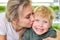 Young mother kisses her happy son against the background of bright shelves with micro greenery