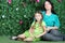 Young mother and little daughter sit on grass in garden