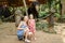 Young mother with little daughter standing near tamed and tied elephants.