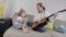 A young mother and a little girl learn to play acoustic guitar sitting at home on the couch.