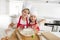 Young mother and little sweet daughter in cook hat and apron cooking together baking at home kitchen