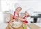 Young mother and little sweet daughter in cook hat and apron cooking together baking at home kitchen