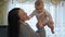 Young mother in the living room, holding a happy newborn toddler boy. Close-up.