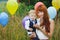 young mother with long red hair holds her son in her arms, the boy has a birthday, the boy is dressed in a suit, balls of