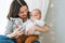 Young mother playing with cute baby boy in bright bedroom, natural tones, love emotion