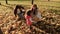 A young mother plays with her daughters collects fallen leaves in an autumn park. family sits on yellow leaves in garden