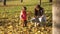 A young mother plays with her daughters collects fallen leaves in an autumn park. family sits on yellow leaves in garden