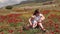 A young mother plays with her little son in a field with flowering poppies.