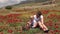 A young mother plays with her little son in a field with flowering poppies.