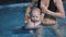 A young mother in the pool of the Wellness centre is engaged in water exercises with his young son.