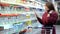 A young mother reads the composition of baby food. A young woman buys baby food in a supermarket. The girl standing at