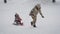 Young mother rolls her daughter on sledding in the park. Winter active family leisure. Cute woman having fun with a girl