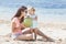 young mother sharing coconut water with her little daughter while sitting on the beach