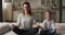Young mother sit on couch teaches little daughter meditating
