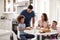 Young mother sitting at table in the kitchen with children, father serving them food, selective focus