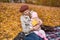 Young mother with small child sitting on picnic blanket on autumn Park background