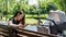 Young mother with smartphone in her hands sitting on bench, next to stroller with baby in Park