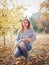 A young mother, squatting in an autumn park and holding a pretty baby in her arms.