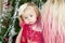 Young mother with a tired baby girl in front of xmas tree. Christmas family portrait.