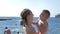 Young mother of a toddler caucasian boy is keeping on her arms and playing with a son on a seaside beach at sunny summer