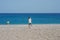 Young mother and toddler son walking towards the blue sea on beautiful pebble beach