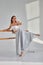 Young motivated woman in skirt stretching legs on ballet barre in studio