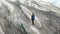 A young mountaineer in sunglasses in a cap and crampons stands on a large glacier with huge cracks in the mountains of