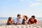 Young multiethnic group of people relaxing on the beach towel near the sea on white sand. Stylish friends hanging on the