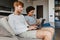 Young multinational couple using laptop and reading book at home