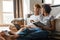 Young multinational couple using laptop and reading book at home