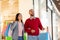 Young multiracial couple posing with bright gift bags, shopping together at huge mall. Sales, retail concept