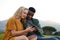 Young multiracial couple sitting and looking down while using mobile phone in field