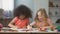 Young multiracial females sitting at the table and drawing with colorful pencils