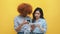Young multiracial friends shopping online using tablet. Afican american and asian women isolated on yellow background