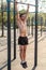 Young muscular athlete doing pull-up exercises hanging with straight arms on a horizontal bar in the park.