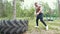 Young muscular man doing exercises workout lifting a huge rubber wheel in the forest