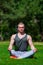Young muscular man is doing yoga in a summer park. Sporty man is sitting in the Lotus position and relaxing outdoors