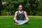 Young muscular man is doing yoga in a summer park. Sporty man is sitting in the Lotus position and relaxing outdoors