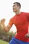 Young muscular man with a red shirt running and listening to music on ear buds outdoors in the park in Beijing, China, with lens