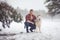 Young muscular man in unbuttoned shirt sits and hugs dog Malamute at walk in winter misty forest.