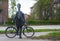 Young musician with a black cello case on his back stands with his bicycle in a suburban street in a residential area on the way