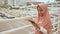 A young Muslim girl in a pink hijab dials a number and talks on the phone over road traffic in the city center.