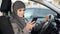 Young Muslim lady sitting in car, scrolling app on phone, searching best route