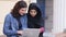 Young muslim woman in black hijab is talking to her female caucasian friend. Two attractive young women sitting outside