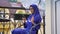 Young muslim woman in hijab sitting in chair on balcony with umbrella and typing on cell phone