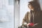 Young Muslim woman sits on the window sill with flower bouquet in hands. Depressed middle-eastern female near the window at home.