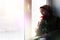 Young Muslim woman sits on the window sill with flower bouquet in hands. Depressed middle-eastern female near the window at home.