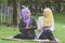 Young muslimah sitting on a green grass at park talking each other and holding a mobile phone