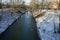 Young mute swans swim along the Wuhle River with snow-covered banks in winter. Berlin, Germany